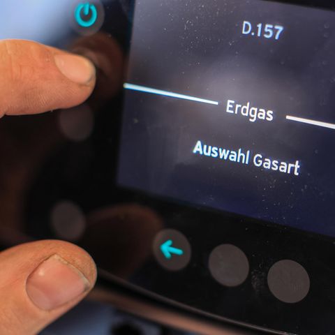 An einer Gasheizung liegen Daumen und Zeigefinger einer linken Männerhand auf einem Display mit Anzeige "Erdgas"