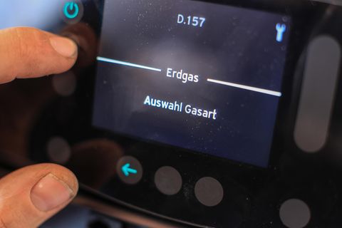 An einer Gasheizung liegen Daumen und Zeigefinger einer linken Männerhand auf einem Display mit Anzeige "Erdgas"