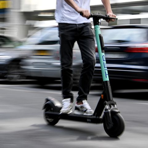 Auf einem E-Scooter fährt ein junger Mann in schwarzen Jeans und weißem T-Shirt durch Berlin