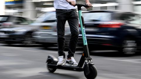 Auf einem E-Scooter fährt ein junger Mann in schwarzen Jeans und weißem T-Shirt durch Berlin