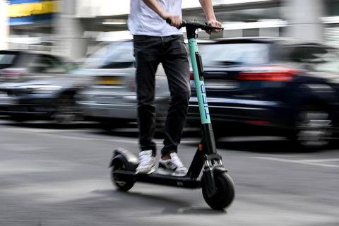 Auf einem E-Scooter fährt ein junger Mann in schwarzen Jeans und weißem T-Shirt durch Berlin