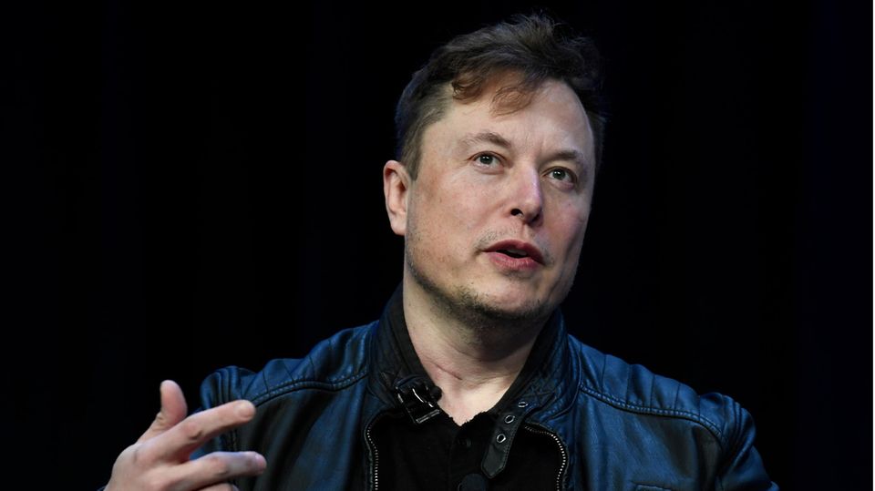 Twitter-Chef Elon Musk gestikuliert, während er auf einer Bühne vor schwarzem Hintergrund spricht