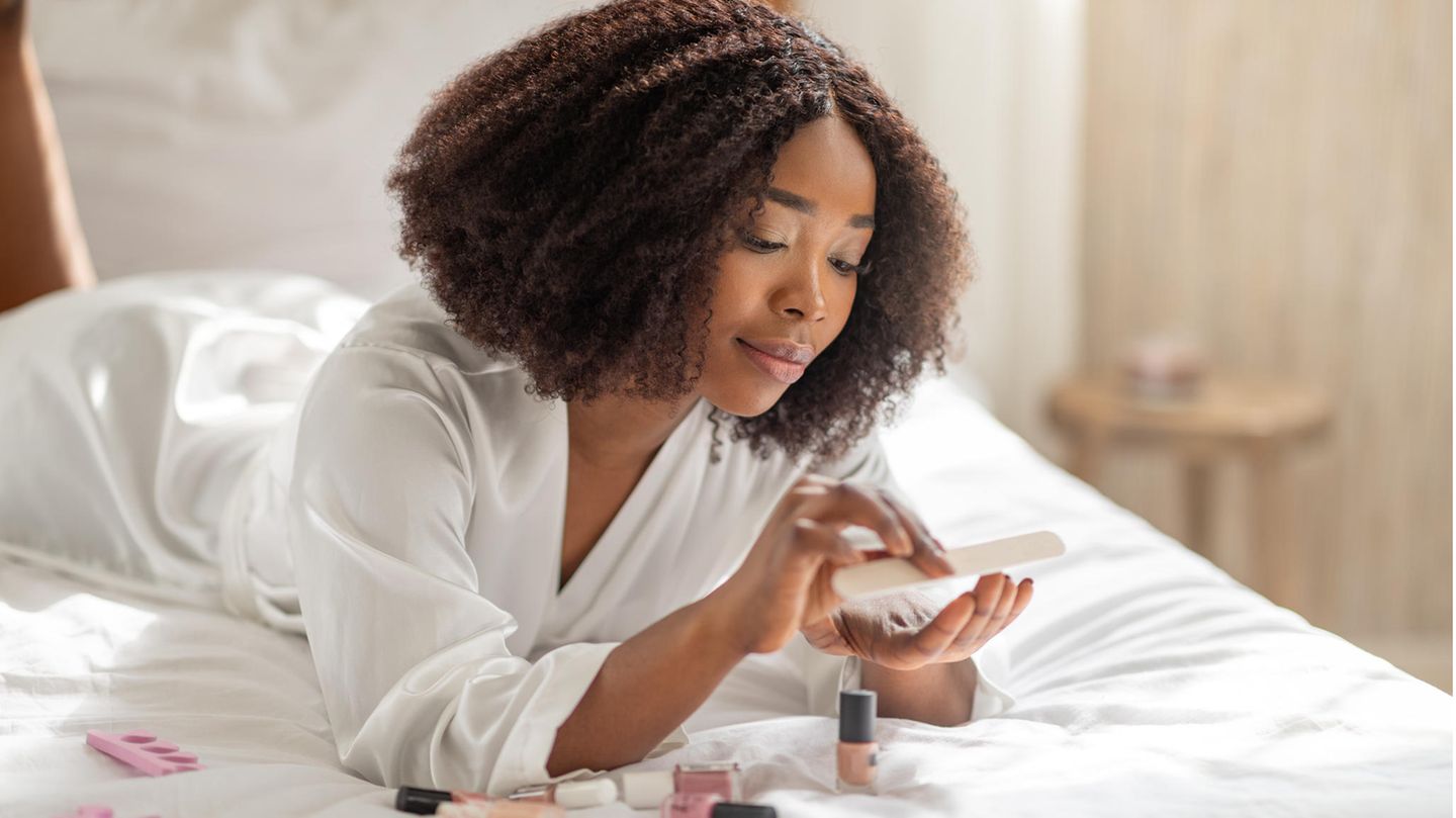 Wie hält mein Nagellack länger? Eine Frau liegt auf dem Bett und feilt ihre Fingernägel.