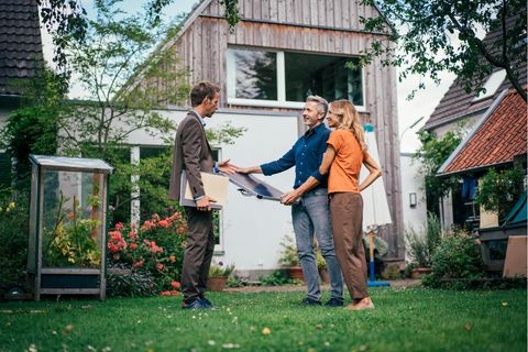 Energetische Sanierung: Ein Paar steht vor ihrem Eigenheim mit einem Energieberater