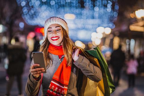 Black Friday Angebote: Lächelnde Frau mit Handy und Einkaufstaschen
