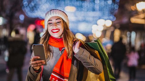Black Friday Angebote: Lächelnde Frau mit Handy und Einkaufstaschen