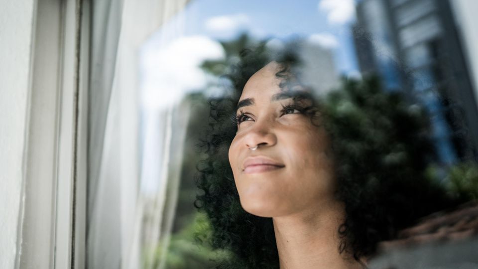 Symbolbild Kinderkriegen: Eine Frau schaut aus dem Fenster. Sie wirkt zufrieden