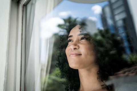 Symbolbild Kinderkriegen: Eine Frau schaut aus dem Fenster. Sie wirkt zufrieden