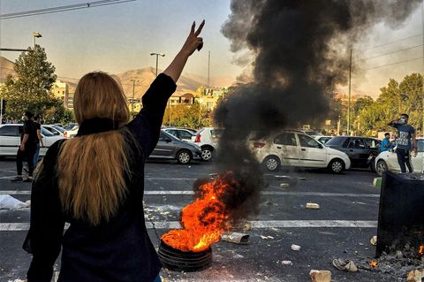 Eine Frau im Iran zeigt das Victory-Zeichen vor einem brennenden Autoreifen