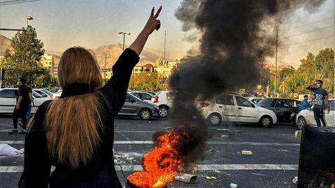 Eine Frau im Iran zeigt das Victory-Zeichen vor einem brennenden Autoreifen