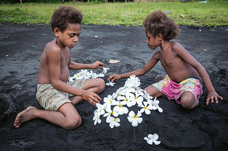 zwei Kinder spielen im dunkelgrauen Sand