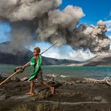 Junge mit Spielzeug vor rauchendem Vulkan