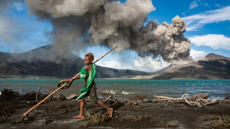Junge mit Spielzeug vor rauchendem Vulkan