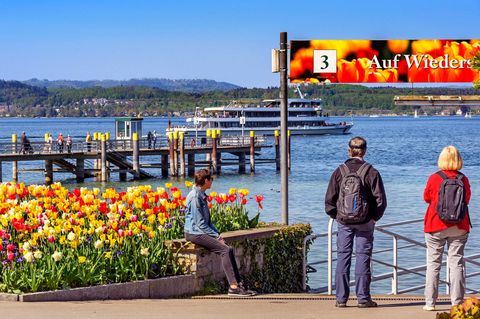 Drei Menschen warten auf der Insel Mainau am Bodensee auf ihr Schiff