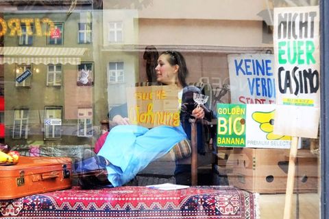 Eine Frau sitzt mit einem Schild, auf dem "Suche Wohnung" steht in einem Schaufenster