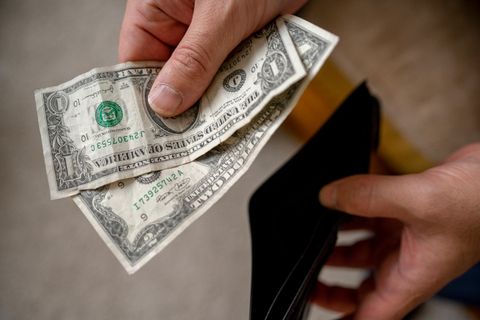 Hand hält zwei Dollarscheine über einem Geldbeutel