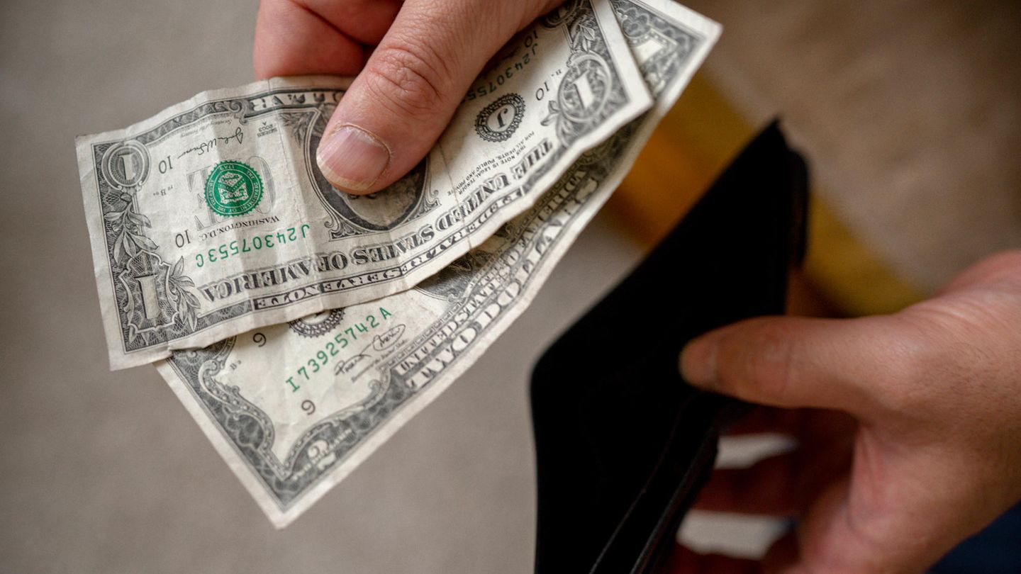 Hand hält zwei Dollarscheine über einem Geldbeutel