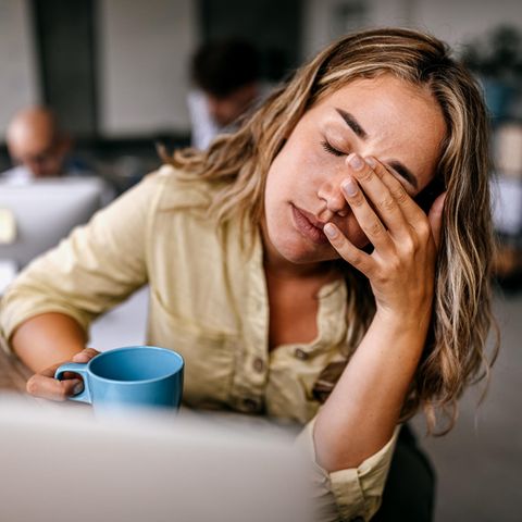 Thema Arbeitssucht: Eine Frau sitzt müde vor ihrem Laptop mit einer Tasse in der Hand