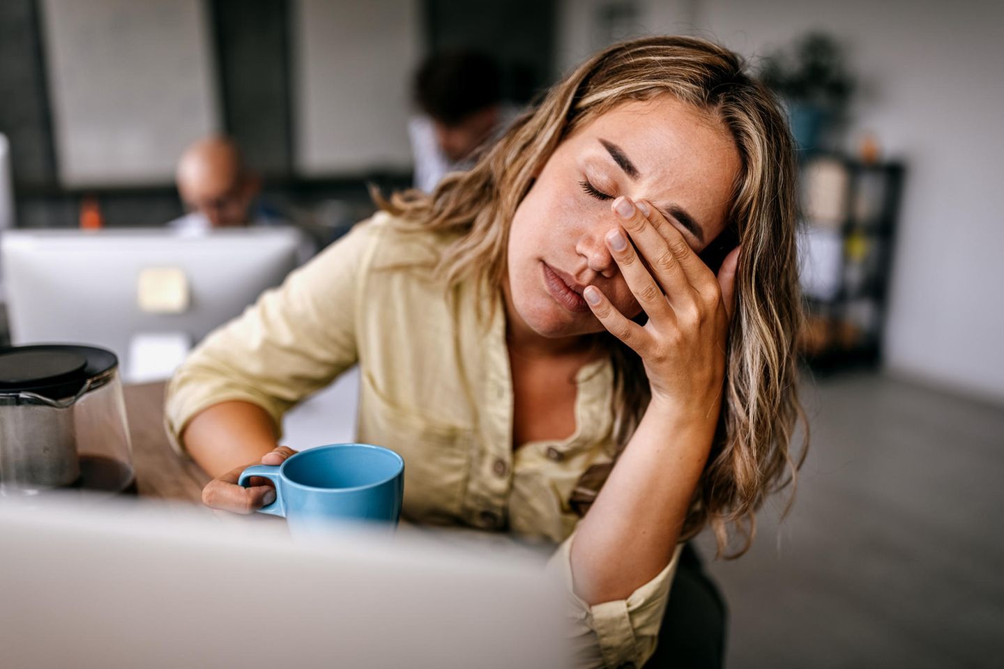 Thema Arbeitssucht: Eine Frau sitzt müde vor ihrem Laptop mit einer Tasse in der Hand