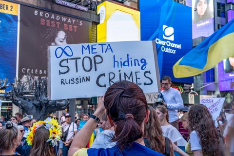 Informationskrieg: Frau hält auf einer Demonstration ein Schild mit der Aufschrift "META stop hiding Russian crimes" hoch
