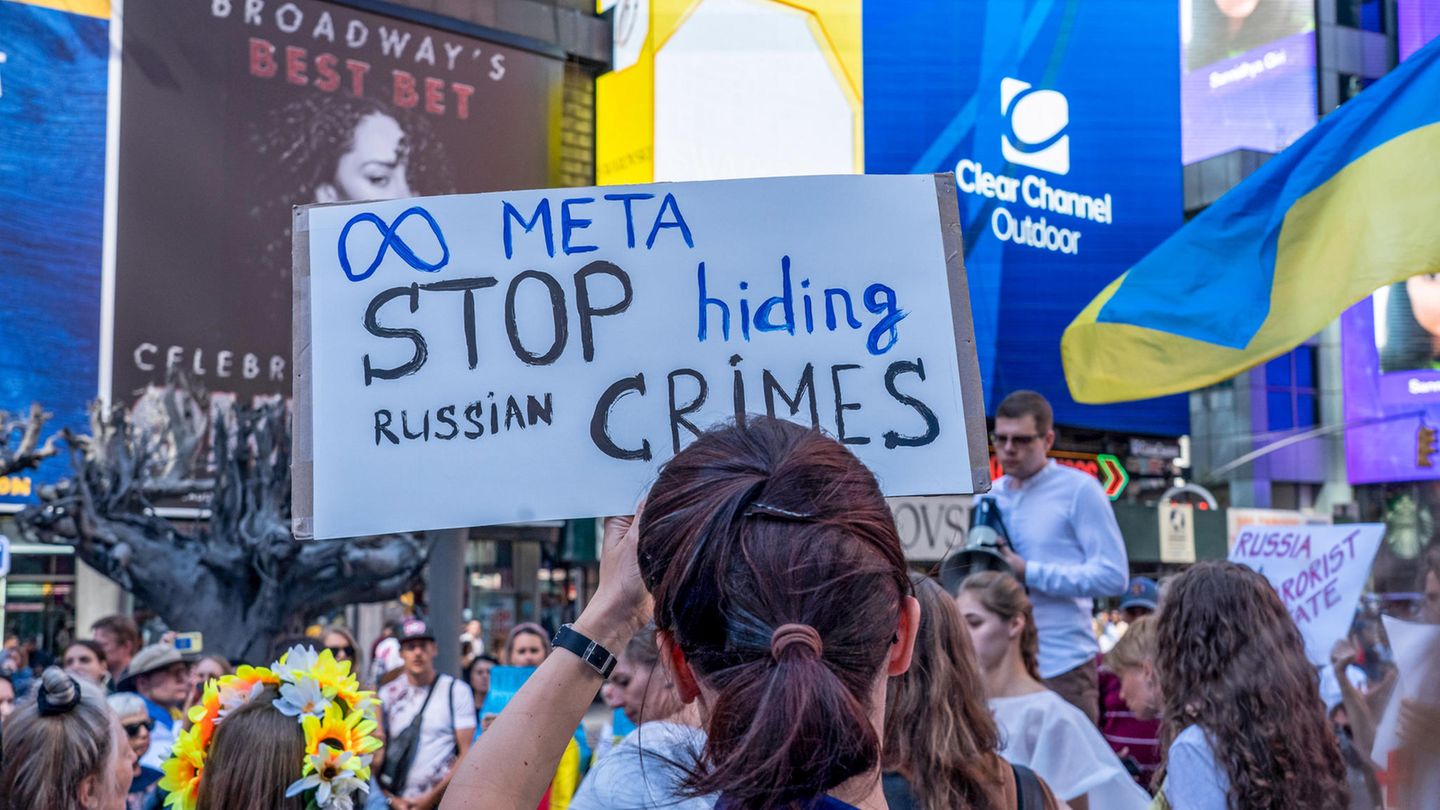 Informationskrieg: Frau hält auf einer Demonstration ein Schild mit der Aufschrift "META stop hiding Russian crimes" hoch