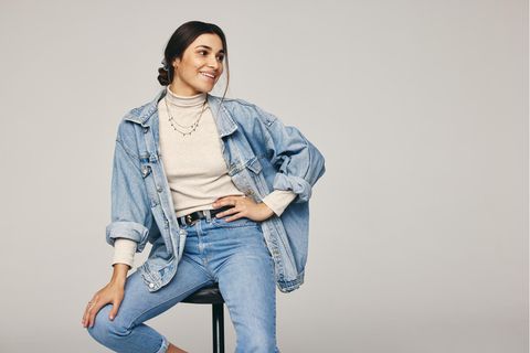 Eine Frau sitzt auf einem Hocker und trägt Jeanshose und -jacke.