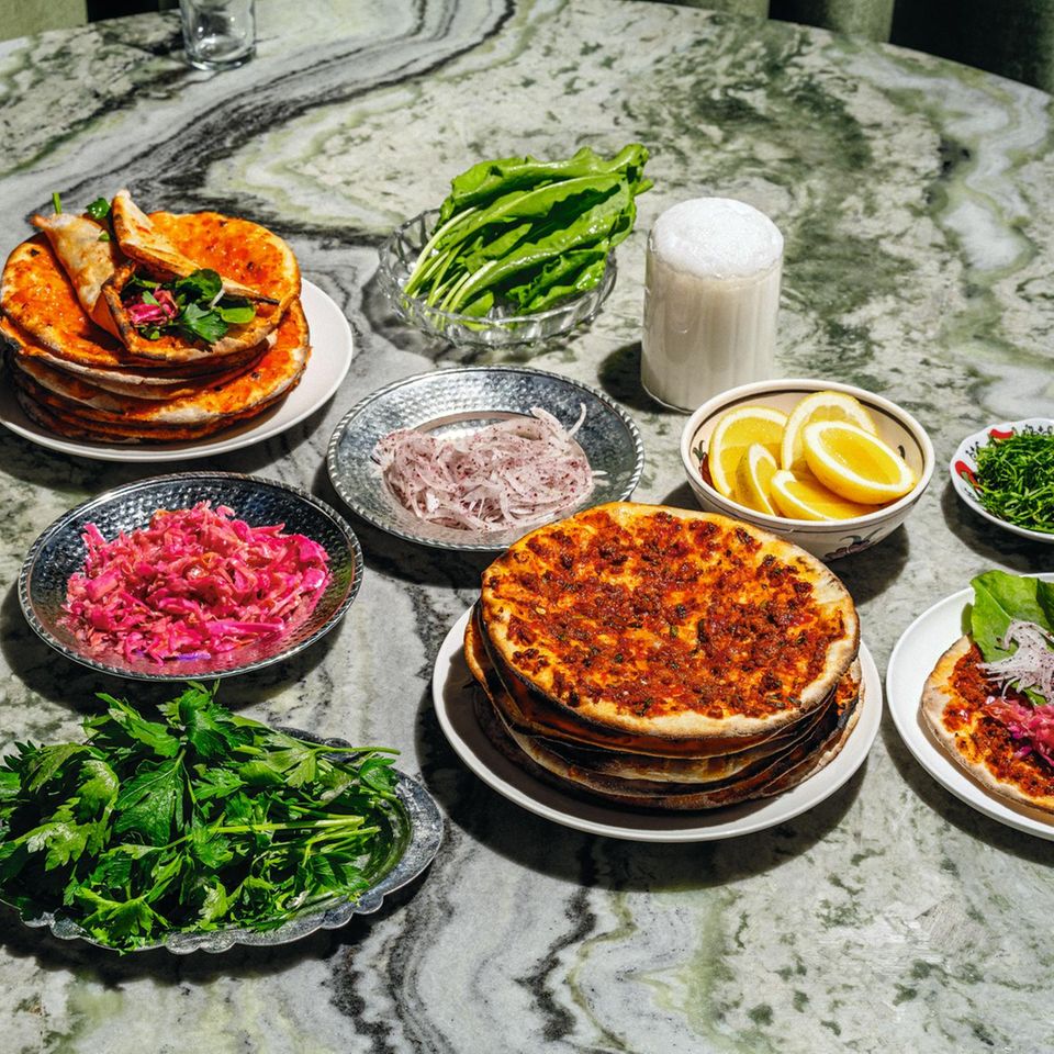 Lahmacun-Express  Zutaten für 18 Stück:  - 345 g Lammhackfleisch, 4 mm (40 % Fett)  - 65 g Biber-Salça  - 65 g Tomaten-Salça  - 5 g Salz  - 6 g gemahlener Kreuzkümmel  - 2 g schwarzer Pfeffer aus der Mühle  - 5 g Pul Biber  - 125 g rote Spitzpaprika (z. B. »Ramiros«)  - 125 g grüne Spitzpaprika (z. B. »Charly«)  - 250 g Tomaten  - 20 g Knoblauch  - 120 g Olivenöl  - 10 g glatte Petersilie, gehackt      Zubereitung:  1. Das Lammhackfleisch mit der Biber- und der Tomaten-Salça sowie allen Gewürzen in einer großen Schüssel gut vermengen. 500 g abwiegen.  2. Die Spitzpaprika entkernen und fein hacken, die Tomaten fein reiben und den Knoblauch schälen und ebenfalls fein reiben. Alles gründlich mit dem Fleisch-Mix vermengen.  3. Dann das Olivenöl und die Petersilie hinzufügen, vermengen und die Masse im Kühlschrank in einem geschlossenen Behälter bis zur Weiterverwendung aufbewahren.      Fertigstellen  - 1 Portion Cüisine-Teig, portioniert à 50 g  Zubereitung:  Vorteig  30 g Wasser  30 g Weißmehl (Weizenmehl; Type 400 oder 405)  1 g frische Hefe (bio)  Alle Zutaten von Hand gut miteinander vermengen. Den Vorteig in einem geschlossenen Behälter 24 Stunden an einem dunklen Ort bei Raumtemperatur gehen lassen.  Hauptteig  61 g Vorteig  355 g lauwarmes Wasser  535 g Weißmehl (Weizenmehl; Type 400 oder 405)  2 g frische Hefe (bio)  10 g Salz  Alle Zutaten außer dem Salz in die Schüssel einer Küchenmaschine geben und mit dem Knethaken auf niedrigster Stufe 8 Minuten kneten lassen. Alternativ das Handrührgerät mit Knethaken verwenden. Das Salz beifügen und weitere 3 Minuten auf der nächsthöheren Stufe kneten lassen.  Den Teig in 50 g oder 100 g schwere Teiglinge portionieren und bis zu 24 Stunden im geschlossenen Behälter (oder zugedeckt, damit der Teig nicht austrocknet) an einem dunklen Ort bei Raumtemperatur aufgehen lassen.      Außerdem:  - Zimmerwarmer Fleisch-Mix  - Mehl zum Ausrollen      Beilagen  - Blumenkohl-Turşu  - Sauerampfer  - Petersilie  - Pivas-Salat  - unbehandelte Zitronen      1. Den Ofen mit einem Backblech bei Ober-/ Unterhitze auf die höchstmögliche Temperatur vorheizen.  2. Einen Teigling von Hand oder mit dem Nudel- holz mithilfe von viel Mehl zu dünnen, runden Fladen ausrollen. Dann so viel Mehl wie möglich wieder von den Teigfladen abklopfen.  3. 50–55 g des Fleisch-Mixes gleichmäßig auf dem Teigfladen verteilen und auf dem heißen Backblech 6–8 Minuten im Ofen knusprig backen, bis der Teig eine goldbraune Farbe annimmt. Aus dem Ofen nehmen.  4. Mit den restlichen 17 Teiglingen wiederholen und mit den Beilagen servieren.