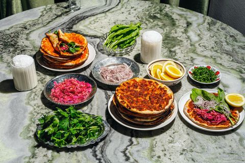 Lahmacun-Express  Zutaten für 18 Stück:  - 345 g Lammhackfleisch, 4 mm (40 % Fett)  - 65 g Biber-Salça  - 65 g Tomaten-Salça  - 5 g Salz  - 6 g gemahlener Kreuzkümmel  - 2 g schwarzer Pfeffer aus der Mühle  - 5 g Pul Biber  - 125 g rote Spitzpaprika (z. B. »Ramiros«)  - 125 g grüne Spitzpaprika (z. B. »Charly«)  - 250 g Tomaten  - 20 g Knoblauch  - 120 g Olivenöl  - 10 g glatte Petersilie, gehackt      Zubereitung:  1. Das Lammhackfleisch mit der Biber- und der Tomaten-Salça sowie allen Gewürzen in einer großen Schüssel gut vermengen. 500 g abwiegen.  2. Die Spitzpaprika entkernen und fein hacken, die Tomaten fein reiben und den Knoblauch schälen und ebenfalls fein reiben. Alles gründlich mit dem Fleisch-Mix vermengen.  3. Dann das Olivenöl und die Petersilie hinzufügen, vermengen und die Masse im Kühlschrank in einem geschlossenen Behälter bis zur Weiterverwendung aufbewahren.      Fertigstellen  - 1 Portion Cüisine-Teig, portioniert à 50 g  Zubereitung:  Vorteig  30 g Wasser  30 g Weißmehl (Weizenmehl; Type 400 oder 405)  1 g frische Hefe (bio)  Alle Zutaten von Hand gut miteinander vermengen. Den Vorteig in einem geschlossenen Behälter 24 Stunden an einem dunklen Ort bei Raumtemperatur gehen lassen.  Hauptteig  61 g Vorteig  355 g lauwarmes Wasser  535 g Weißmehl (Weizenmehl; Type 400 oder 405)  2 g frische Hefe (bio)  10 g Salz  Alle Zutaten außer dem Salz in die Schüssel einer Küchenmaschine geben und mit dem Knethaken auf niedrigster Stufe 8 Minuten kneten lassen. Alternativ das Handrührgerät mit Knethaken verwenden. Das Salz beifügen und weitere 3 Minuten auf der nächsthöheren Stufe kneten lassen.  Den Teig in 50 g oder 100 g schwere Teiglinge portionieren und bis zu 24 Stunden im geschlossenen Behälter (oder zugedeckt, damit der Teig nicht austrocknet) an einem dunklen Ort bei Raumtemperatur aufgehen lassen.      Außerdem:  - Zimmerwarmer Fleisch-Mix  - Mehl zum Ausrollen      Beilagen  - Blumenkohl-Turşu  - Sauerampfer  - Petersilie  - Pivas-Salat  - unbehandelte Zitronen      1. Den Ofen mit einem Backblech bei Ober-/ Unterhitze auf die höchstmögliche Temperatur vorheizen.  2. Einen Teigling von Hand oder mit dem Nudel- holz mithilfe von viel Mehl zu dünnen, runden Fladen ausrollen. Dann so viel Mehl wie möglich wieder von den Teigfladen abklopfen.  3. 50–55 g des Fleisch-Mixes gleichmäßig auf dem Teigfladen verteilen und auf dem heißen Backblech 6–8 Minuten im Ofen knusprig backen, bis der Teig eine goldbraune Farbe annimmt. Aus dem Ofen nehmen.  4. Mit den restlichen 17 Teiglingen wiederholen und mit den Beilagen servieren.