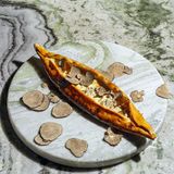 Pide mit Trüffel und Traubendicksaft  Zutaten:  1 Portion Cüisine-Teig, geviertelt  Zubereitung:  Vorteig  30 g Wasser  30 g Weißmehl (Weizenmehl; Type 400 oder 405)  1 g frische Hefe (bio)  Alle Zutaten von Hand gut miteinander vermengen. Den Vorteig in einem geschlossenen Behälter 24 Stunden an einem dunklen Ort bei Raumtemperatur gehen lassen.  Hauptteig  61 g Vorteig  355 g lauwarmes Wasser  535 g Weißmehl (Weizenmehl; Type 400 oder 405)  2 g frische Hefe (bio)  10 g Salz  Alle Zutaten außer dem Salz in die Schüssel einer Küchenmaschine geben und mit dem Knethaken auf niedrigster Stufe 8 Minuten kneten lassen. Alternativ das Handrührgerät mit Knethaken verwenden. Das Salz beifügen und weitere 3 Minuten auf der nächsthöheren Stufe kneten lassen.  Den Teig in 50 g oder 100 g schwere Teiglinge portionieren und bis zu 24 Stunden im geschlossenen Behälter (oder zugedeckt, damit der Teig nicht austrocknet) an einem dunklen Ort bei Raumtemperatur aufgehen lassen.      Für den Belag:  - 300 g Pide-Käsemischung (100 g Cheddar, 100 g Emmentaler, 400 g Frischkäse, 300 g Salzlakenkäse)  - 300 g Trüffel-Brie  - Weißmehl (Weizenmehl) zum Ausrollen  - Traubendicksaft  - frischer Trüffel, min. 10 g pro Person      Zubereitung:  1. Den Ofen mitsamt zwei Backblechen bei Ober-/Unterhitze auf die höchstmögliche Temperatur vorheizen.  2. Die Teiglinge von Hand mithilfe von viel Mehl flach drücken und mit einem Nudelholz zu ovalen Fladen ausrollen, dann so viel Mehl wie möglich wieder von den Teigfladen abklopfen.  3. Die Käsemischung gleichmäßig auf den Fladen verteilen, sodass auf allen Seiten ein Rand von etwa 1 cm frei bleibt. Dann den Trüffel-Brie punktuell mithilfe eines Löffels darauf verteilen.  4. Die Pides im vorgeheizten Ofen auf den heißen Backblechen 15–20 Minuten knusprig ba- cken, bis sie eine goldbraune Farbe annehmen.  5. Die fertig gebackenen Pides aus dem Ofen nehmen und den Rand üppig mit Traubendicksaft bepinseln. Den Trüffel sofort darüberhobeln und die Pides heiß servieren.