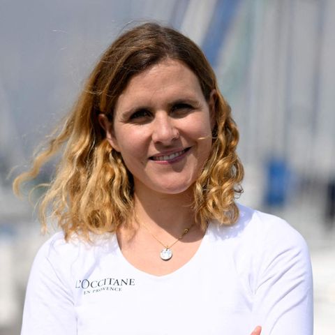 Clarisse Crémer, eine weiße, blonde Frau steht in weißem Langarmshirt in einem Yachthafen und lächelt in die Sonne