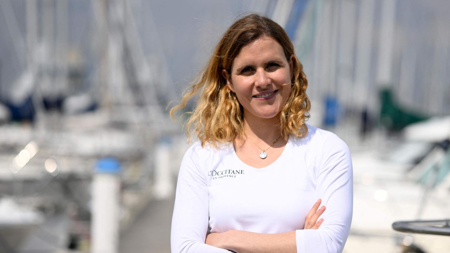Clarisse Crémer, eine weiße, blonde Frau steht in weißem Langarmshirt in einem Yachthafen und lächelt in die Sonne