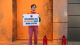 Ein Klimaaktivist der Letzten Generation posiert vor der orangenen Prada-Fassade. Auf einem Schild steht: "Wir können uns die Reichen nicht mehr leisten."