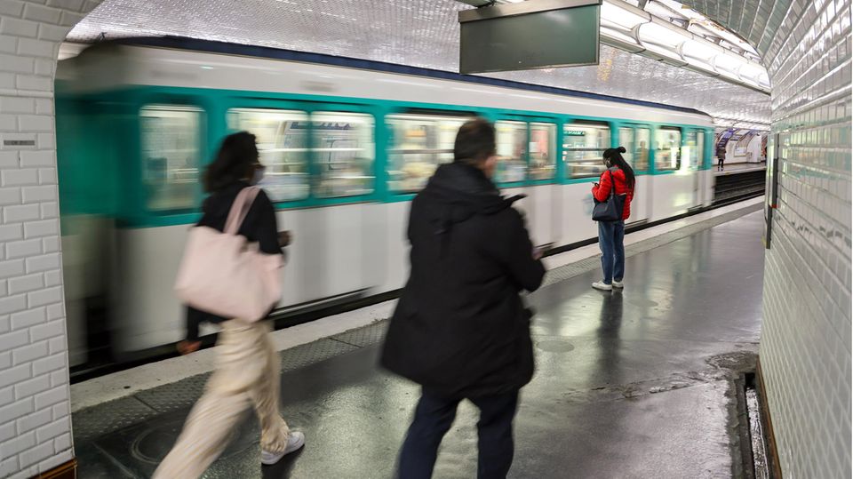 In Paris gehen zwei Menschen auf einen Bahnsteig der Metro zu, wo gerade ein weiß-grüner Zug einfährt