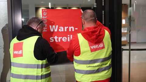 Streikende befestigen ein Plakat mit der Aufschrift "Warnstreik" am BER Airport