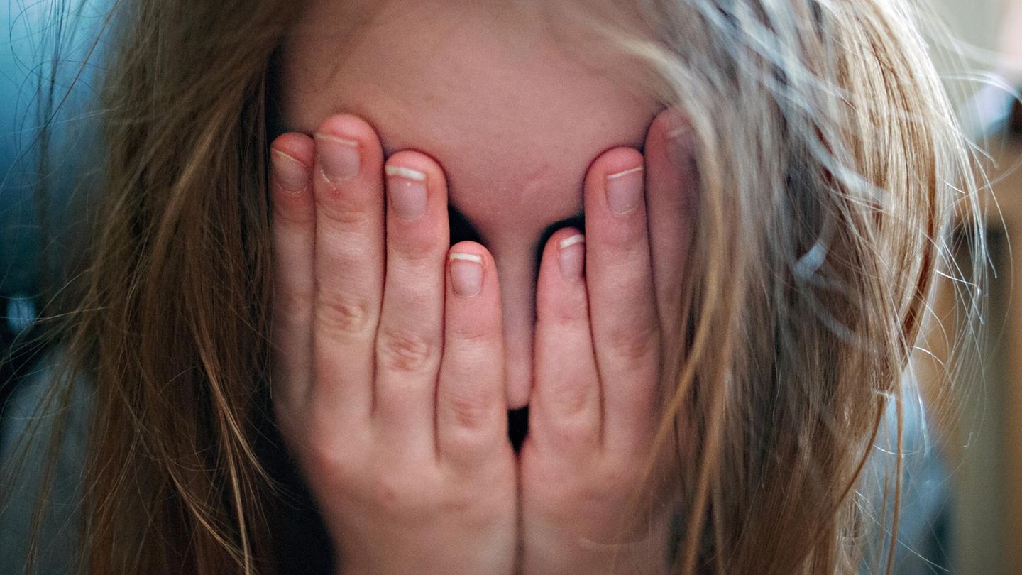 Depression bei Kindern: Ein junges Mädchen hält sich die Hände vor ihr Gesicht