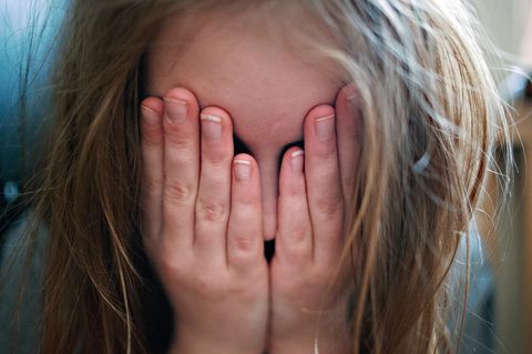 Depression bei Kindern: Ein junges Mädchen hält sich die Hände vor ihr Gesicht