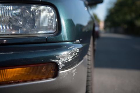 Ein grüner älterer Golf steht mit weißen Lackspuren an der Ecke seiner vorderen Stoßstange auf einem Parkplatz