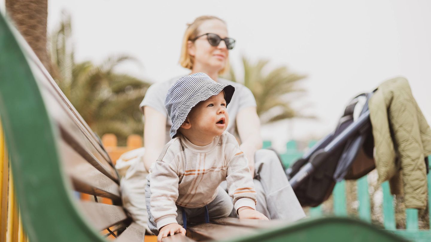 Frau sitzt mit Baby auf der Parkbank