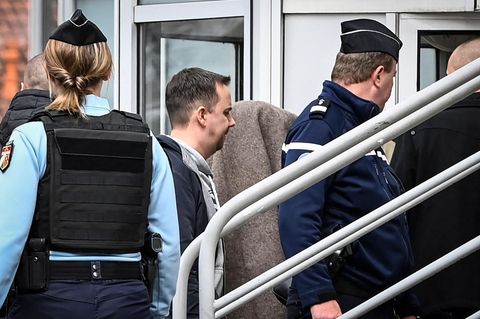 Zwischen blau uniformierten Polizistinnen und Polizisten geht ein Mensch unter einer grau-braunen Decke