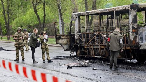 Ukraine, Donezk: Eine Journalistin spricht mit Ermittlern, während diese an einem nach Beschuss verbrannten Bus arbeiten.