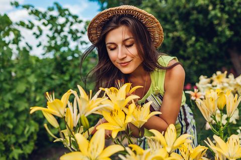 Eine Frau steht im Garten und riecht an Blumen