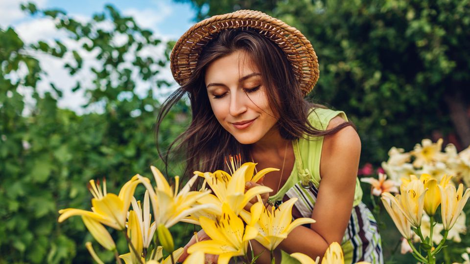 Eine Frau steht im Garten und riecht an Blumen