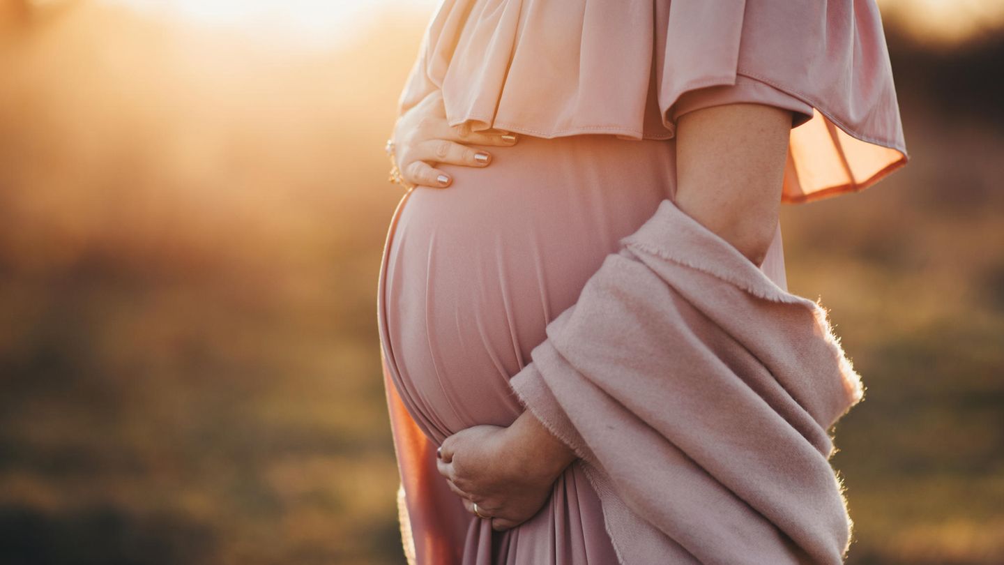 Eine schwangere Frau steht im Feld mit einem schicken Kleid