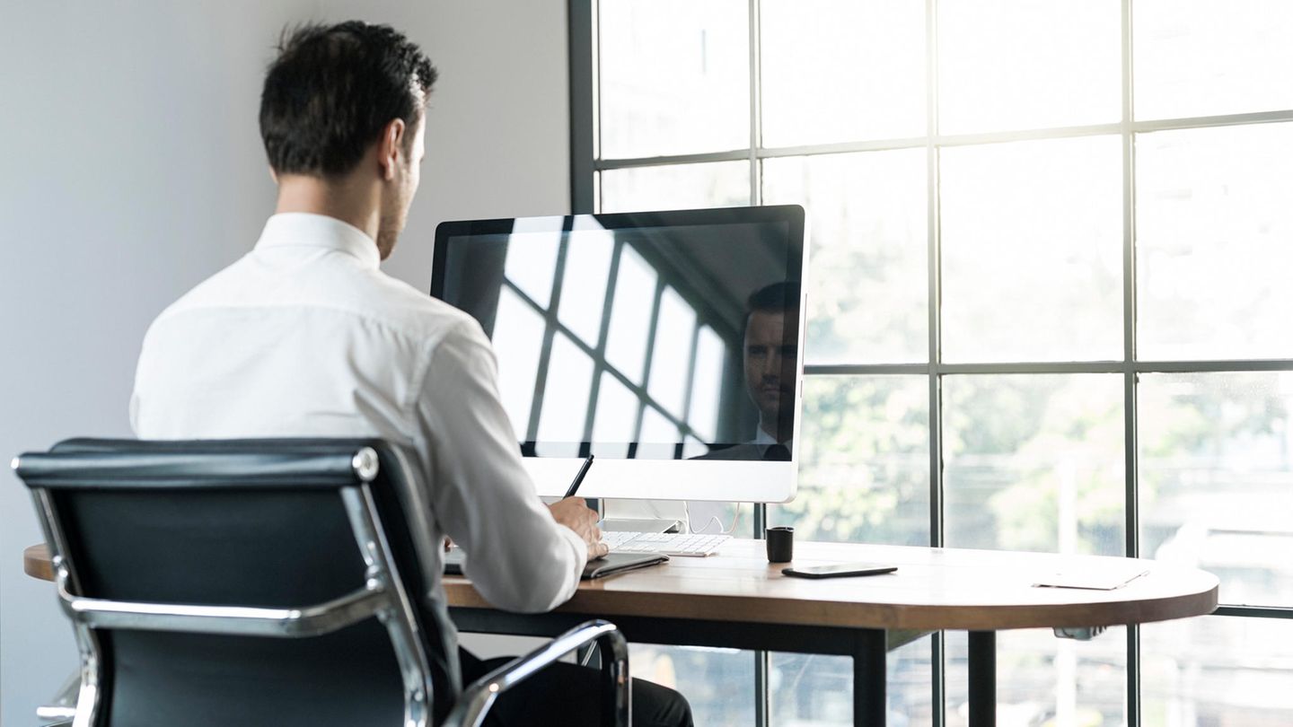 Ein Mann sitzt auf einem Bürostuhl vor einem Monitor an einem Schreibtisch