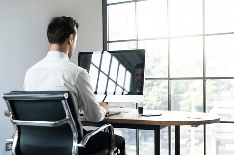 Ein Mann sitzt auf einem Bürostuhl vor einem Monitor an einem Schreibtisch