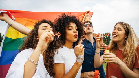 Menschen machen Seifenblasen vor einer Regenbogenflagge