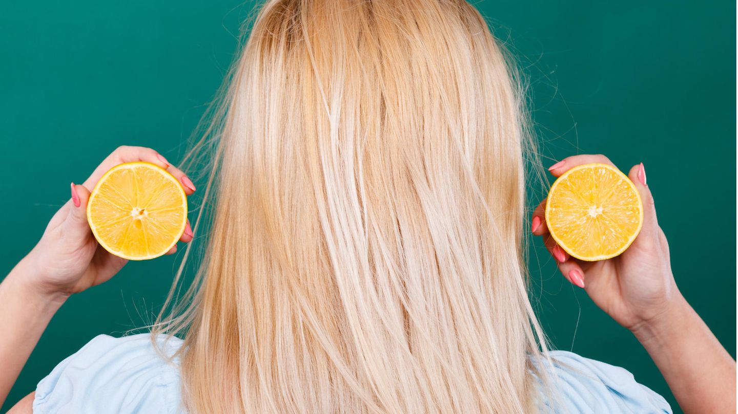 Eine blonde Frau hält Zitronen neben ihr Haar.