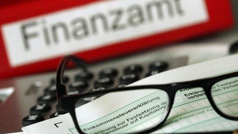 Auf einem Formular für die Steuererklärung liegt eine Brille, dahinter ein Schild mit der Aufschrift "Finanzamt"