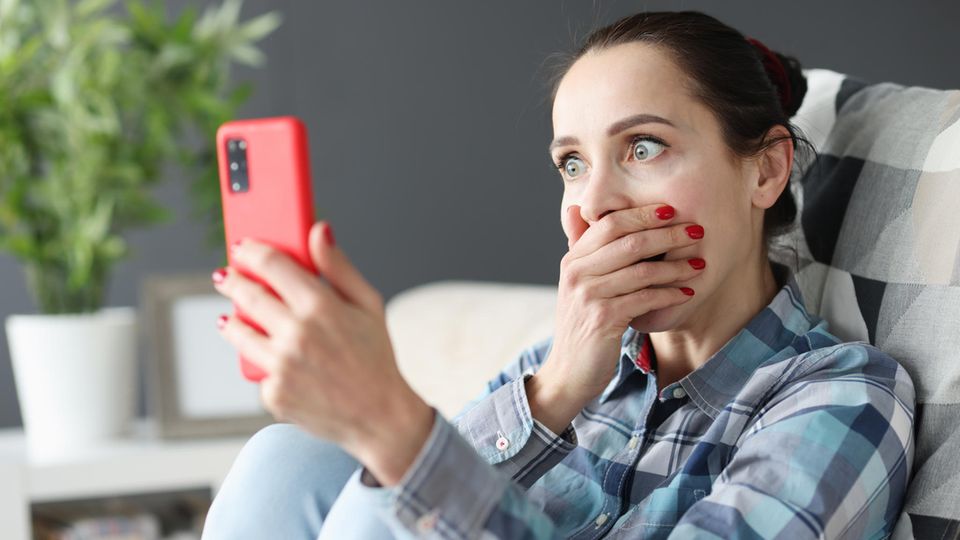 Frau schaut schockiert auf ihr Whatsapp-Smartphone