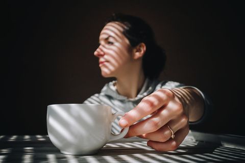 Thema Kopfschmerzen: Eine Frau mit einer Tasse Kaffee vor sich